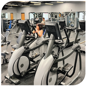workout room with elliptical machines and people working out