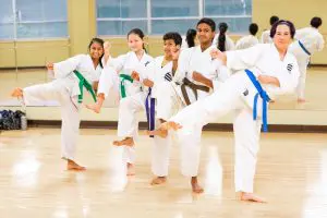4 kids and an instructor in front of a mirror at martial art class posing kicks